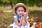 Little girl in straw hat picking apples in green grass background. Child Girl with red apple in summer orchard. Harvest concept. S