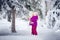 A little girl on the street in winter stands on a tree and shakes off fresh snow from the spruce branches