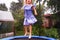 little girl in a striped dress jumps on a trampoline.