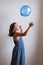 Little girl in summer dress with arms in the air throwing a blue balloon
