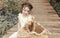 Little girl in summer dress sitting outside on wooden path in front of straw basket with rabbits