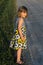 Little girl in summer dress standing next to a dirt road with worried expression