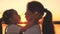 A little girl at sunset kisses a happy mother holding her in her arms. A child with his beloved mother plays at dawn in