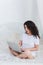 A little girl surprised with a laptop sitting on a bed in front of a white background