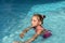 A little girl swimming in a bright turquoise water of a pool