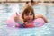 Little girl swimming in pool using inflatable circle and showing thumb up