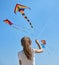 The little girl in t-shirt plays on the beach by the sea with a colorful kite. In the background many people are walking on