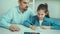 Little girl is about to cry while doing homework together with strict father