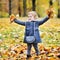 Little girl tossing leaves in autumn park