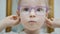 Little girl tries fashion medical glasses near mirror - shopping in ophthalmology clinic