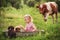 A little girl in a trough on a green meadow bathes little puppies. In the background, a cow grazes. Simple rural farm spiritual lo