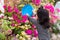 Little girl using a blue bowl is watering a pink flower called bougainvillea. Water the plants in front of the house.