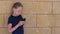 Little girl using phone and standing near beige stone wall