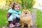 Little girl walking, training a dog in the autumn park. child playing with pomeranian outdoors.