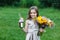 Little girl walks alone in a meadow with flowers and drinks juice