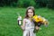 Little girl walks alone in a meadow with flowers and drinks juice