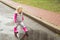 A little girl walks through dirty puddles in pink boots, rainy autumn