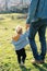 Little girl walks through a green meadow, holding her dad hand. Cropped. Back view