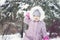 little girl in a warm coat and a hood plays snowballs in a snow fortress