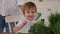 A little girl waves her hand standing near a table with micro-greenery at home.