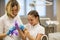 Little girl wear medical gloves with the help of a dentist woman in dental clinic