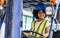 Little girl wearing hard hat, driving tractor in factory, smiling, playing alone as worker with happiness, doing activities on