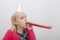 Little girl wearing party hat blowing noisemaker at home