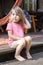 Little girl wearing pink t-shirt sitting on wooden stairs on patio, summer season