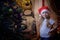 Little girl wearing red cap at home in the room decorating for Christmas or New year. Dark pictures with female child