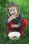 Little girl wearing red gumboots taking ripe raspberries from white bowl to her mouth