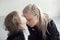 Little girl in white dress with artificial black wings kisses her mother in the forehead