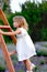 Little girl in a white dress climbs a wooden staircase in nature