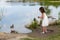 Little girl in white dress feeding ducks at the pond