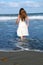 Little Girl in White Dress Steps Into Ocean as Wave Rolls In