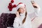 A little girl in a white sweater and Santa Claus hat looks at a mobile phone and says hello. Girl talking by video call