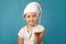 Little girl with a white towel on her head washes her face on a blue background. The child has foam on his hand.