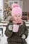 A little girl in winter clothes with a cup of hot cocoa with marshmallows, in the courtyard of a country house decorated