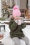 A little girl in winter clothes with a cup of hot cocoa with marshmallows, in the courtyard of a country house decorated