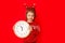 A little girl in winter clothes holds a watch on a red background. New year`s concept, space for text