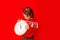 A little girl in winter clothes holds a watch on a red background. New year`s concept, space for text