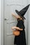 Little girl in a witch costume knocking on the door, trick or treating