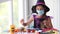 A little girl in a witch costume in a medical mask plays a bat with a craft.