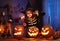 Little girl in witch hat and skeleton costume with magic wand in hand with frightening face