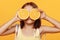 A little girl in a yellow dress, on an orange background, balks, closes her eyes with oranges.