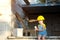 Little girl in a yellow hardhat is playing builder on the construction site of her future home. Expectation of moving, choosing a