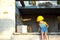 Little girl in a yellow hardhat is playing builder on the construction site of her future home. Expectation of moving, choosing a