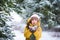 A little girl in a yellow jacket plays with snow in the winter. The child holds the snow in his hands