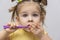 little girl in a yellow shirt is brushing her clean teeth and covers her mouth with her hand