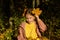 Little girl in yellow sweatshirt and dusty mauve coat is sitting in autumn forest, putting yellow leaves in her braids.