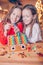 Little girls making Christmas gingerbread house at fireplace in decorated living room.